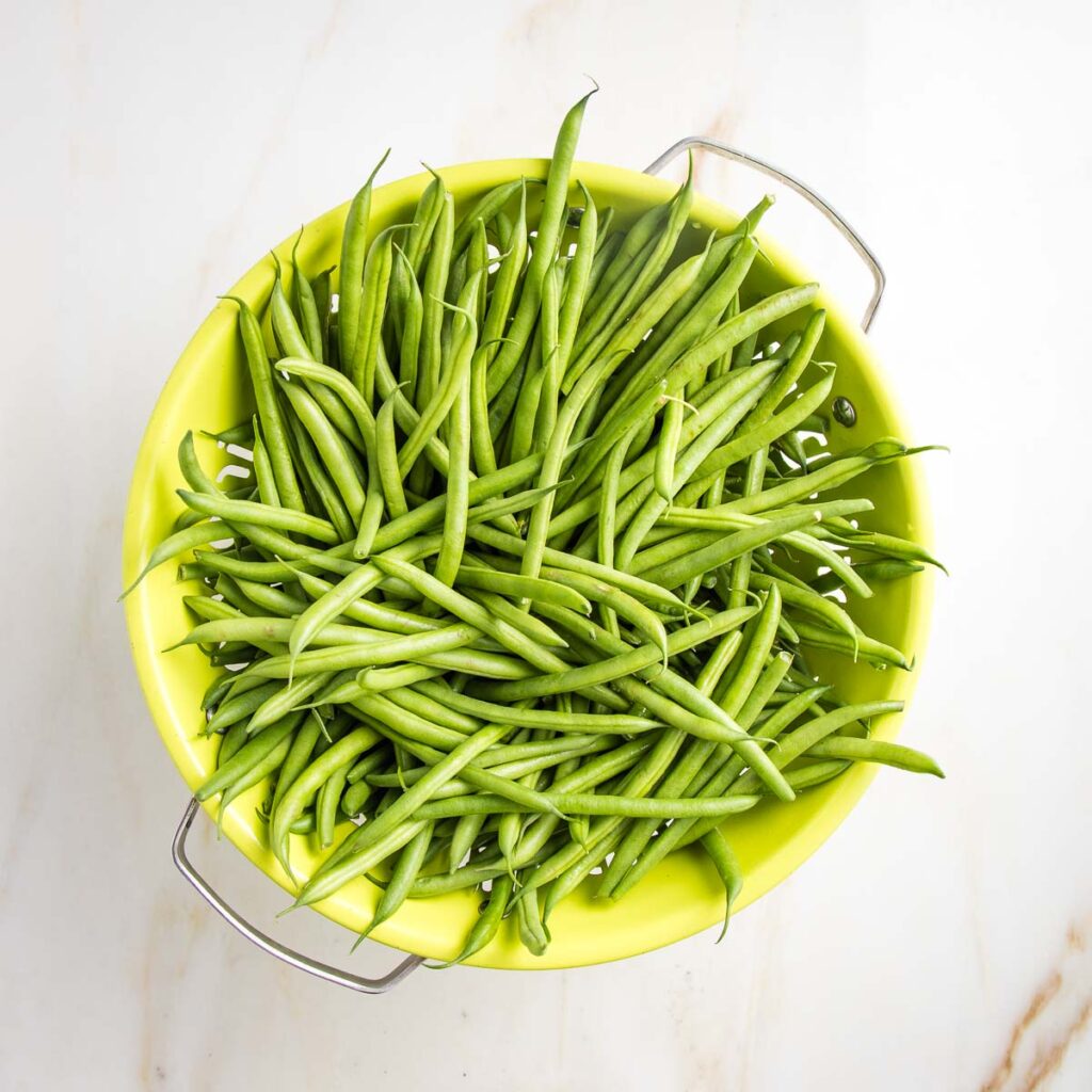 Lime green colander filled with green beans.
