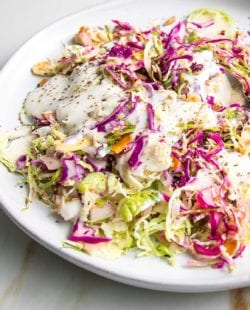 Shredded brussels sprouts and cabbage salad with creamy dairy-free dressing on a white plate, sprinkled with toasted nuts and seeds
