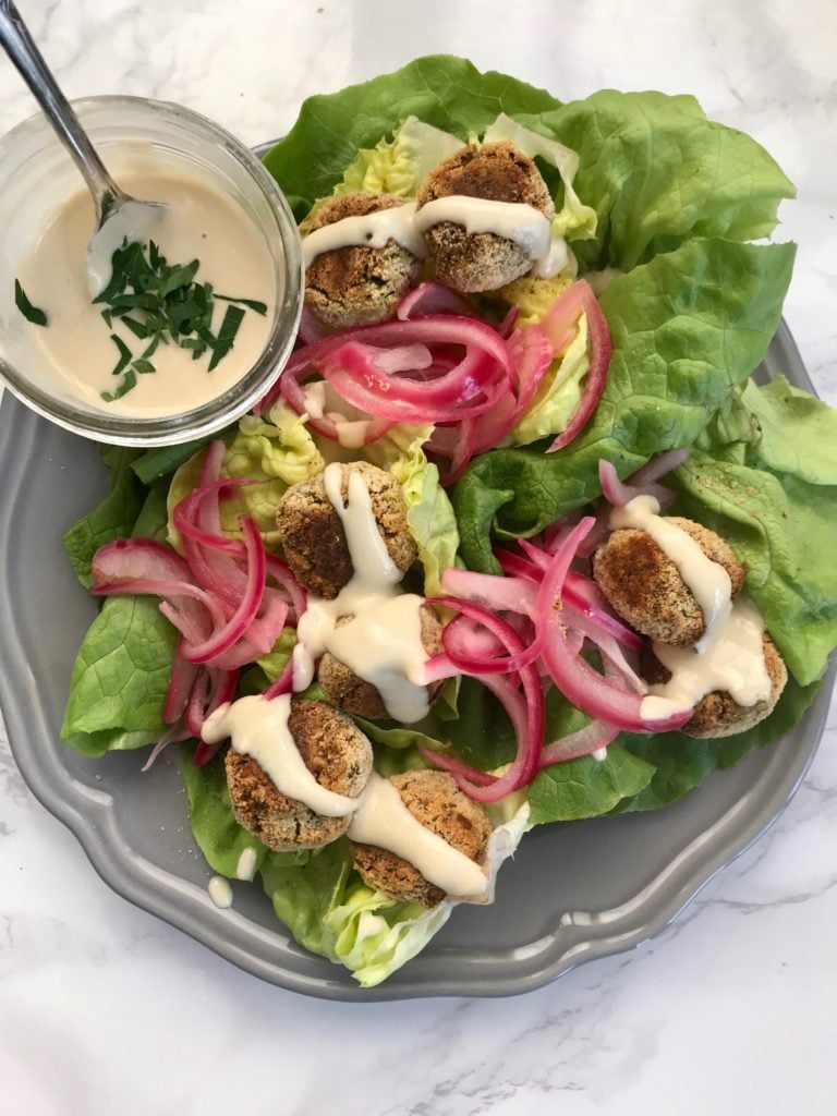 Bright pink pickled onions and creamy tahini drizzle with falafel on top of bright green lettuce.