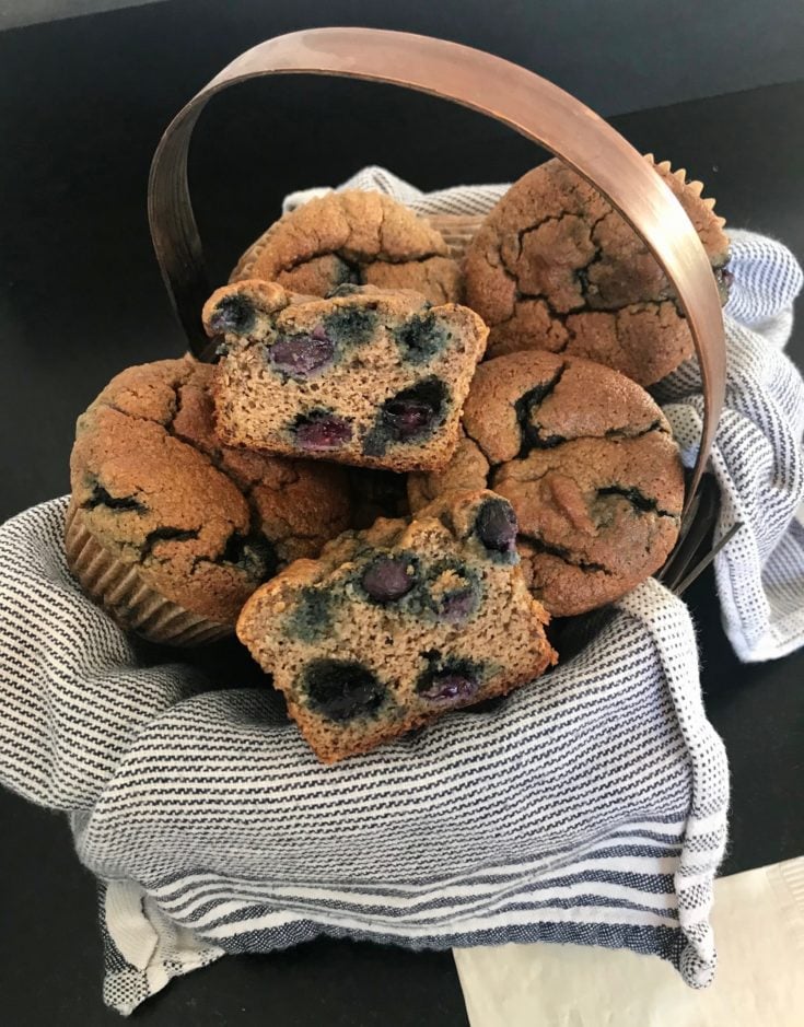 Tea towel lined basket filled with blueberry muffins.
