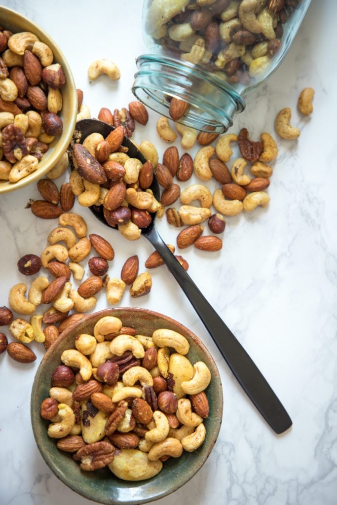 Spiced nuts, spilling out of a jar on the counter and filled into small bowls.