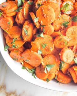 bottom left corner of white bowl with carrot rounds sprinkled with green parsley.