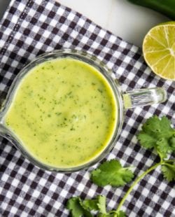 Black and White checkered napkin with a glass pitcher of avocado dressing plus cilantro and lime.