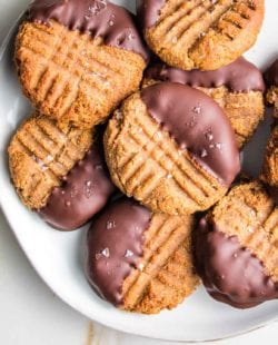 White plate loaded with peanut butter cookies that have been dipped in chocolate.