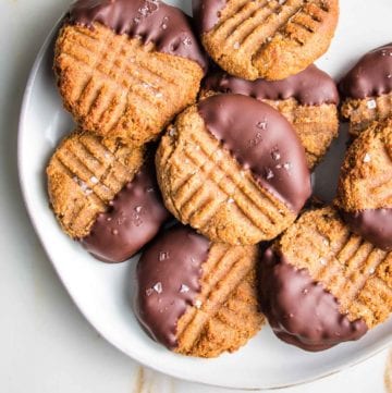 White plate loaded with peanut butter cookies that have been dipped in chocolate.