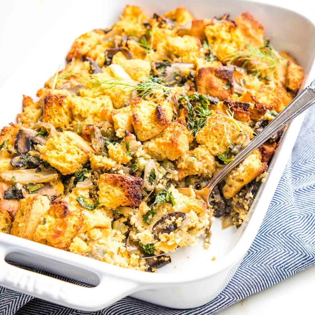 White casserole dish filled with cornbread stuffing, including mushrooms, kale, celery and fresh herbs.