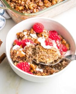 Bowl with quinoa breakfast bake, topped with yogurt and almond butter. Sprinkled with chopped walnuts and fresh raspberries