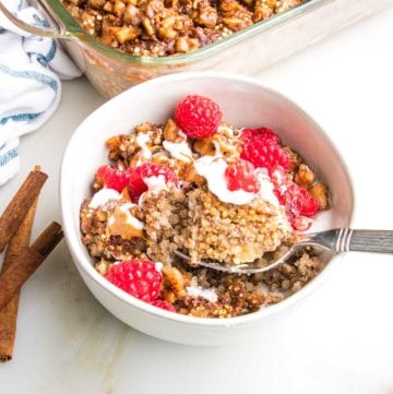 Bowl with quinoa breakfast bake, topped with yogurt and almond butter. Sprinkled with chopped walnuts and fresh raspberries