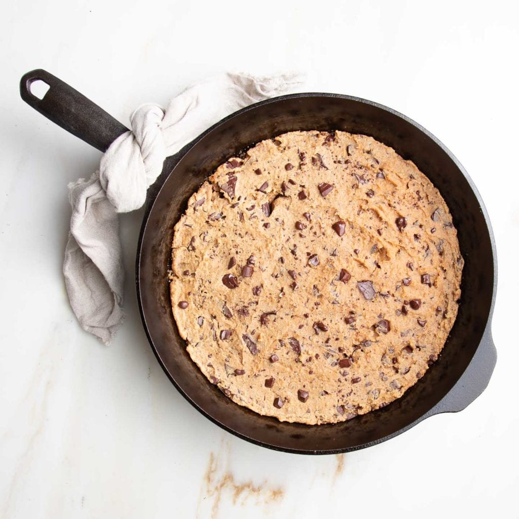 Cast iron skillet with chocolate chunk cookie baked into it. An ivory linen napkin tied onto the skillet handle.
