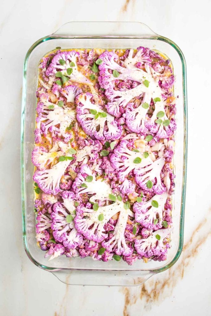 Purple cauliflower thinly sliced and placed on the top of a casserole dish filled with cauliflower kugel, ready to bake.