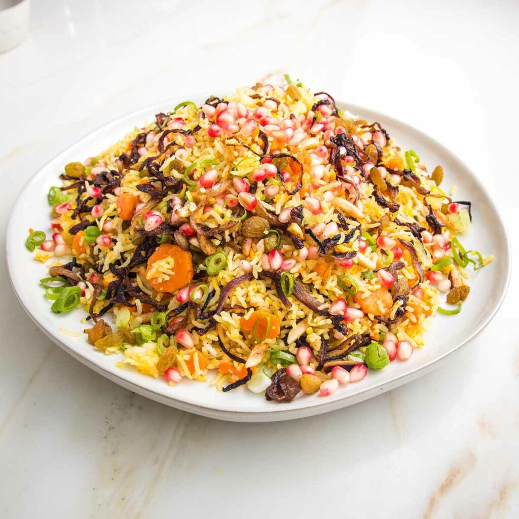 White rimmed plate filled with jeweled rice: rice, carrots, raisins, caramelized onions, almonds, scallions.