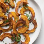 Round plate with half moon shaped roasted delicata squash sprinkled with parsley.