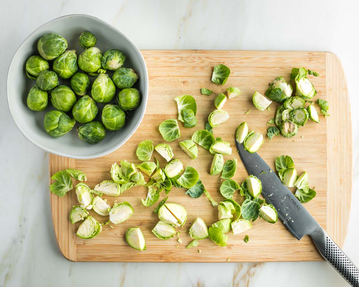 Bowl of brussels sprouts, and trimming them on wooden board before cutting into quarters. 