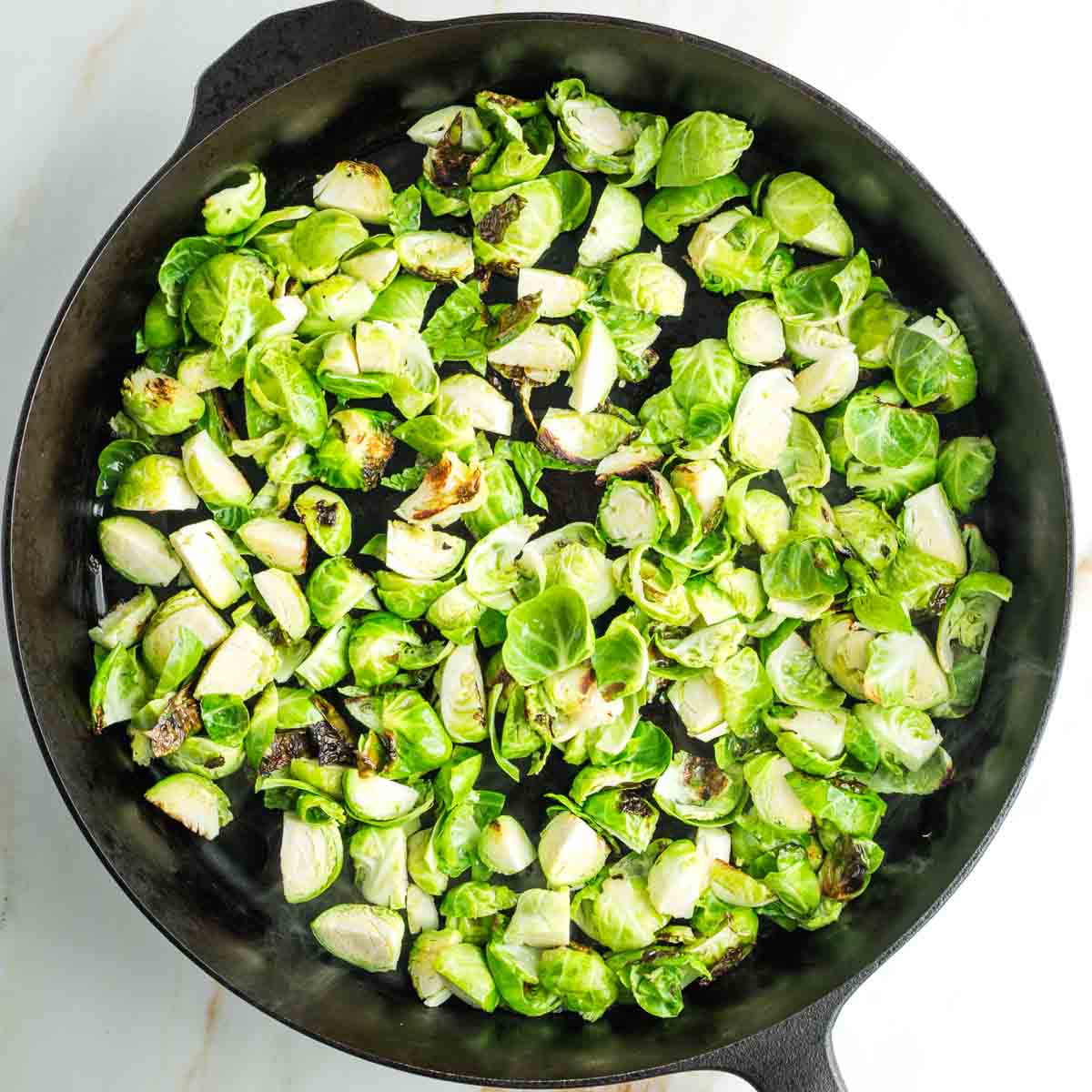 Quartered Brussels sprouts in a cast iron skillet, a few starting to crisp up. 