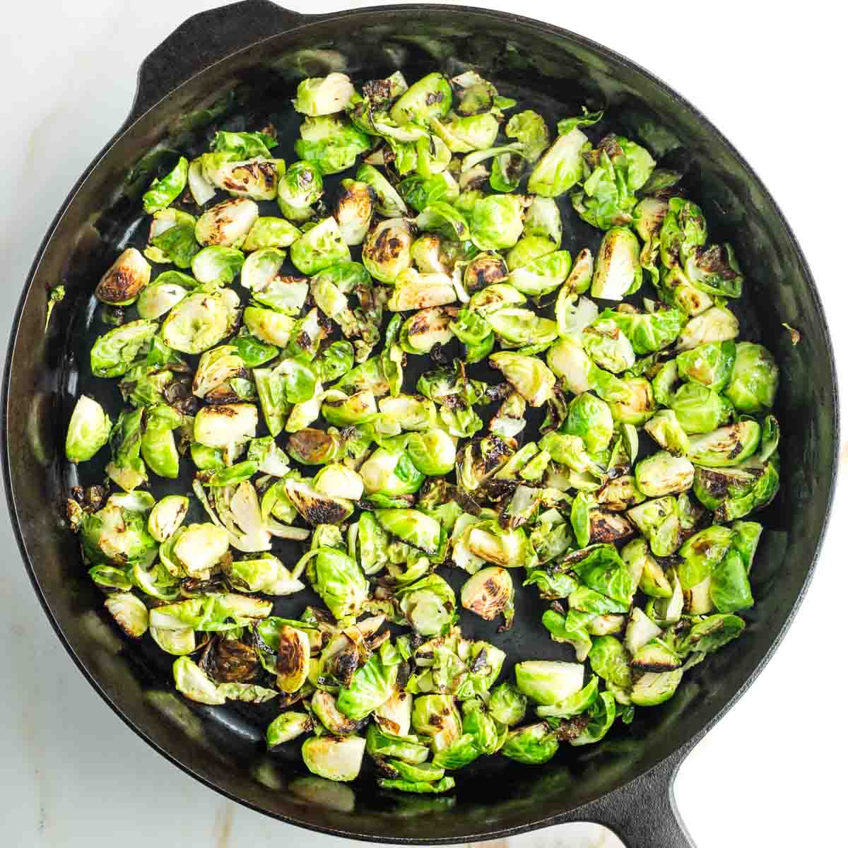 Crispy pieces of Brussels sprouts in a cast iron skillet. 