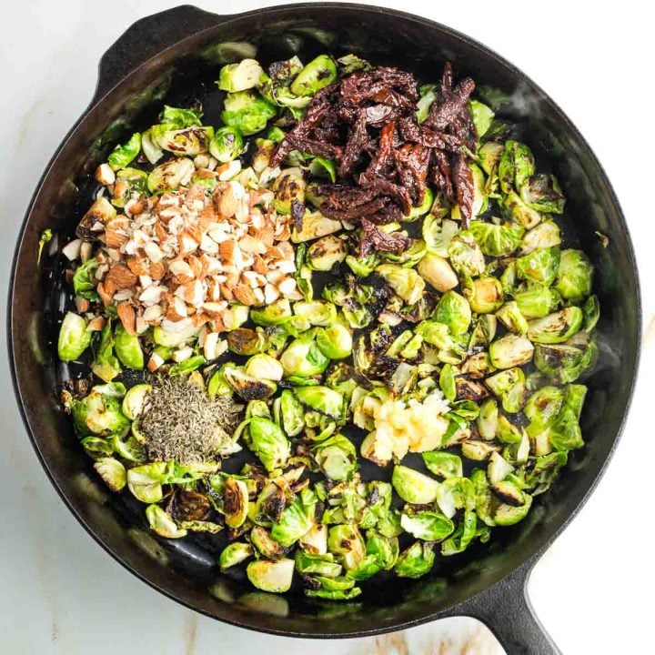 Crispy Brussels sprouts in a skillet with chopped almonds, spices, garlic and sun dried tomato strips.