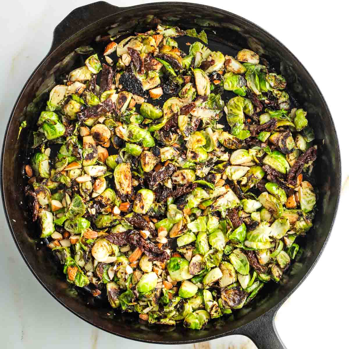 Cast iron skillet with crispy Brussels sprouts, almonds and sun dried tomato strips. 