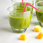 Small glass with bright green smoothie and pink straw.