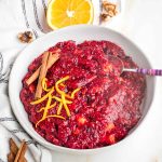 Bowl of chunky cranberry sauce with orange peel and cinnamon sticks.