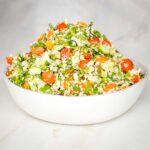Bowl of tabbouleh with colorful tomatoes, fresh herbs, scallions and riced parsnips.