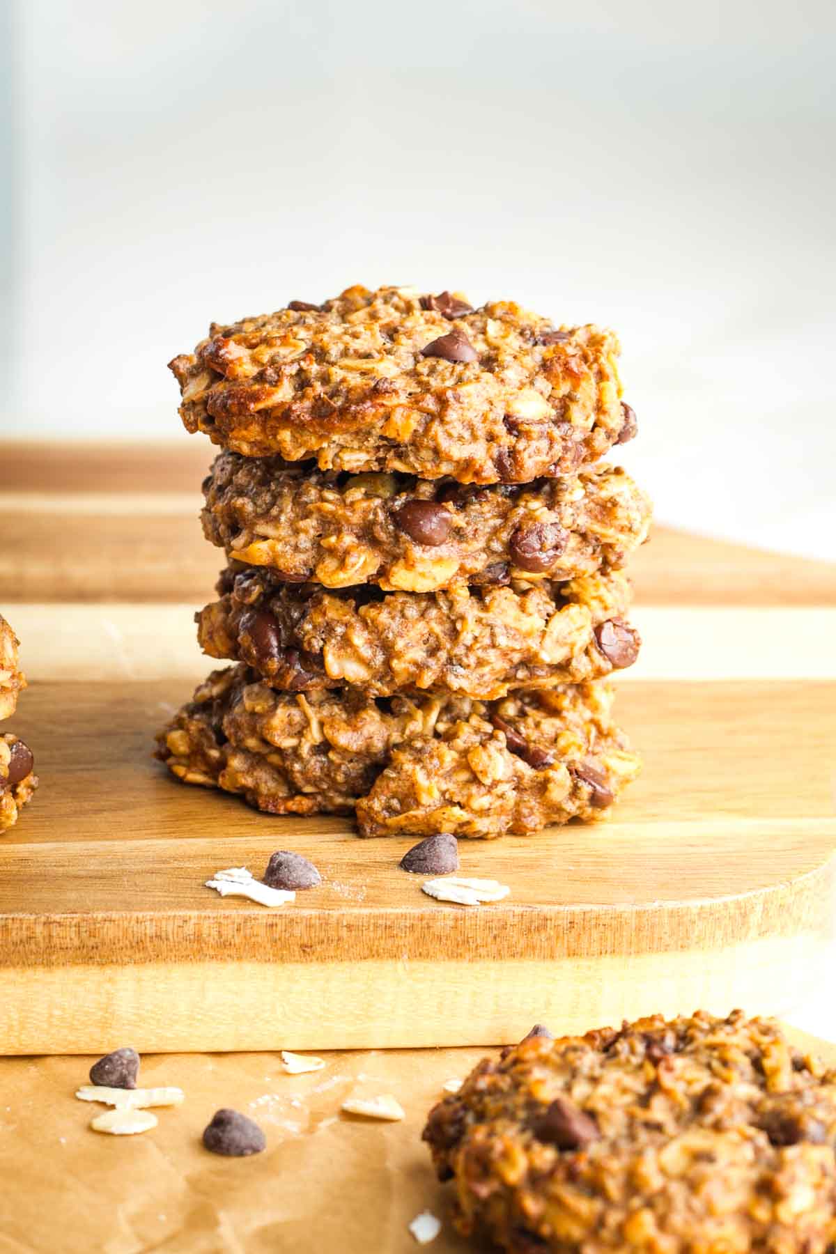 Stack of banana chocolate chip cookies piled 4 high on a wooden board. 