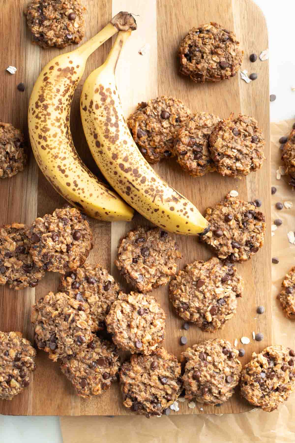 Chocolate chip oatmeal cookies on a board with 2 ripe bananas. 