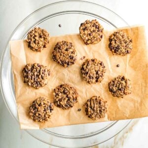 Chocolate chip oatmeal banana cookies on a piece of parchment on a glass pedestal.