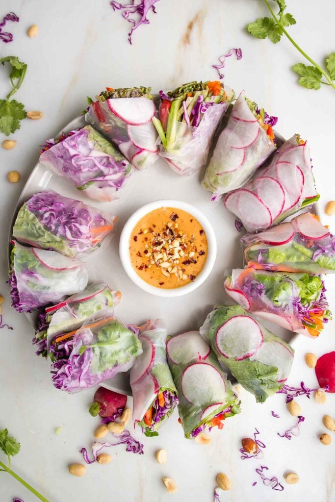 Circular arrangement of colorful fresh rolls with a dish of peanut sauce in the center.