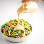Pouring creamy garlic dressing over a simple, colorful, salad.