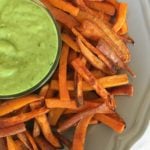 Crispy sweet potato fries on a grey plate with a dish of avocado dressing in the center.