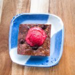 brownie on a bright blue plate with raspberry sauce on top.