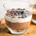 Chocolate chia pudding in a glass, topped with cream and blueberries.