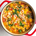 Chunky minestrone soup with veggies, beans, pasta and wilted kale in a dutch oven.