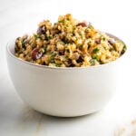 Cauliflower rice with olives, pine nuts and parsley in a white bowl.