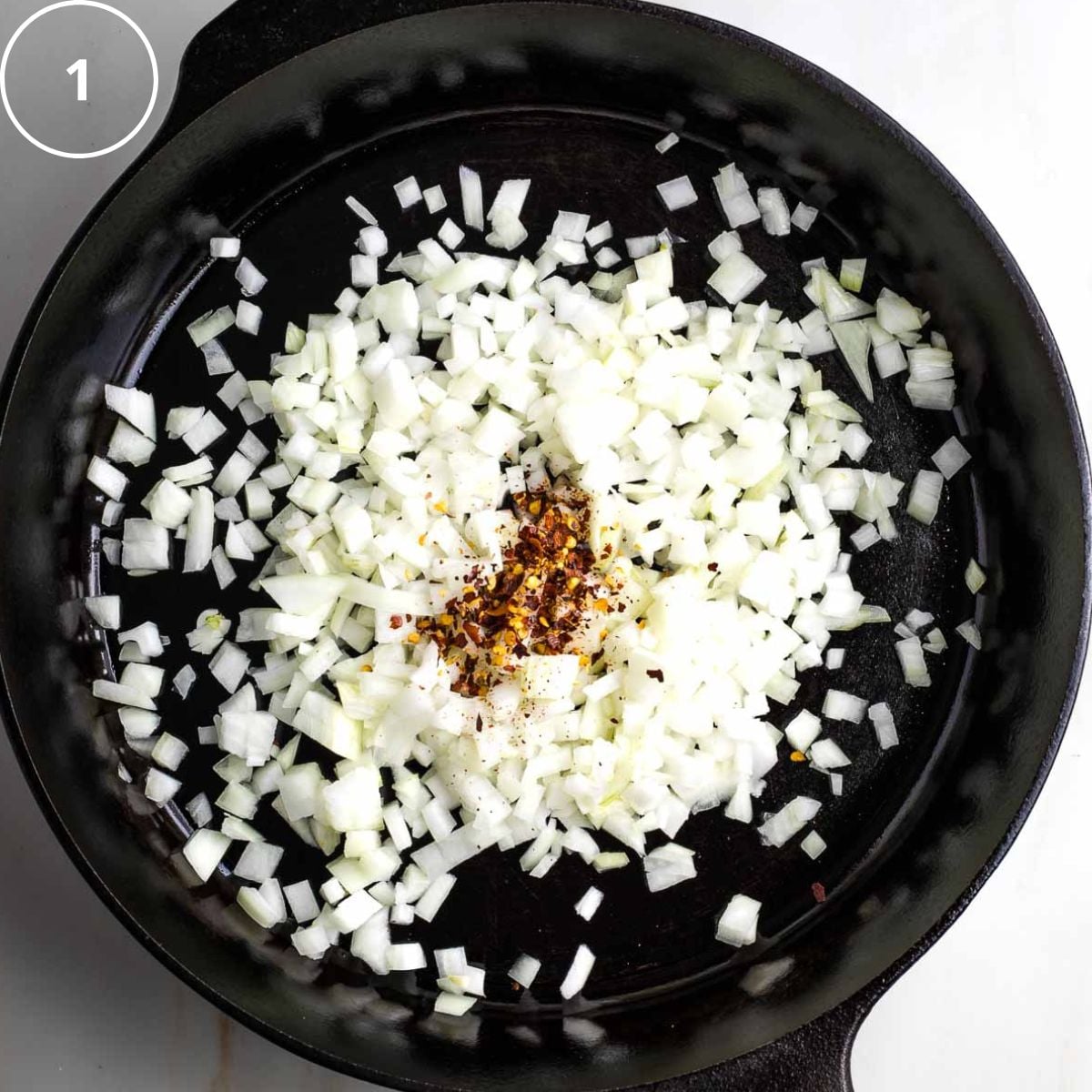 Cast iron skillet with diced onions and crushed red pepper.