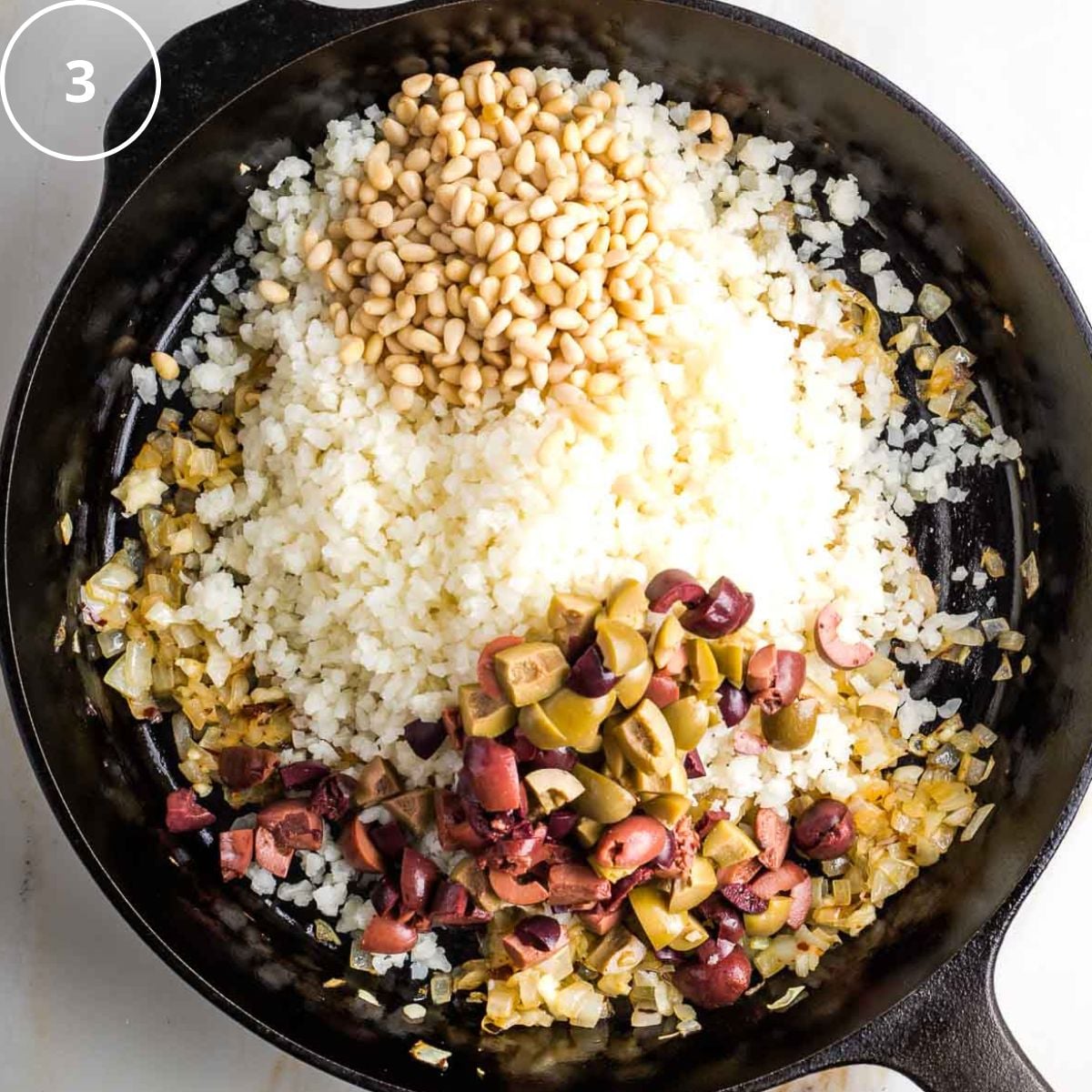 Cast iron skillet with riced cauliflower, chopped olives and pine nuts over satueed onions.