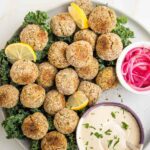 plate filled with baked falafel balls, tahini sauce and small bowl of pickled onions.