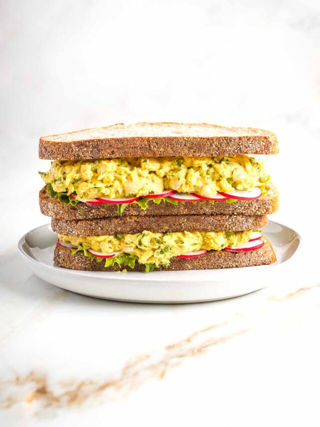 Stacked sandwiches filled with vegan curried chicken salad, lettuce and red radish slices.