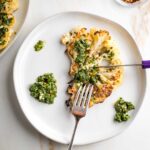 Cutting a cauliflower steak with chimichurri sauce with a steak knife.