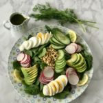 Sliced boiled eggs, avocado, cucumbers, and pine nuts on a bed of spinach
