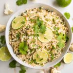 Cauliflower Rice with lime slices and cilantro in a white, low shallow bowl.