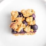 Close up of one blueberry crumble bar. You can see the jam and the fresh blueberries through the crispy top.