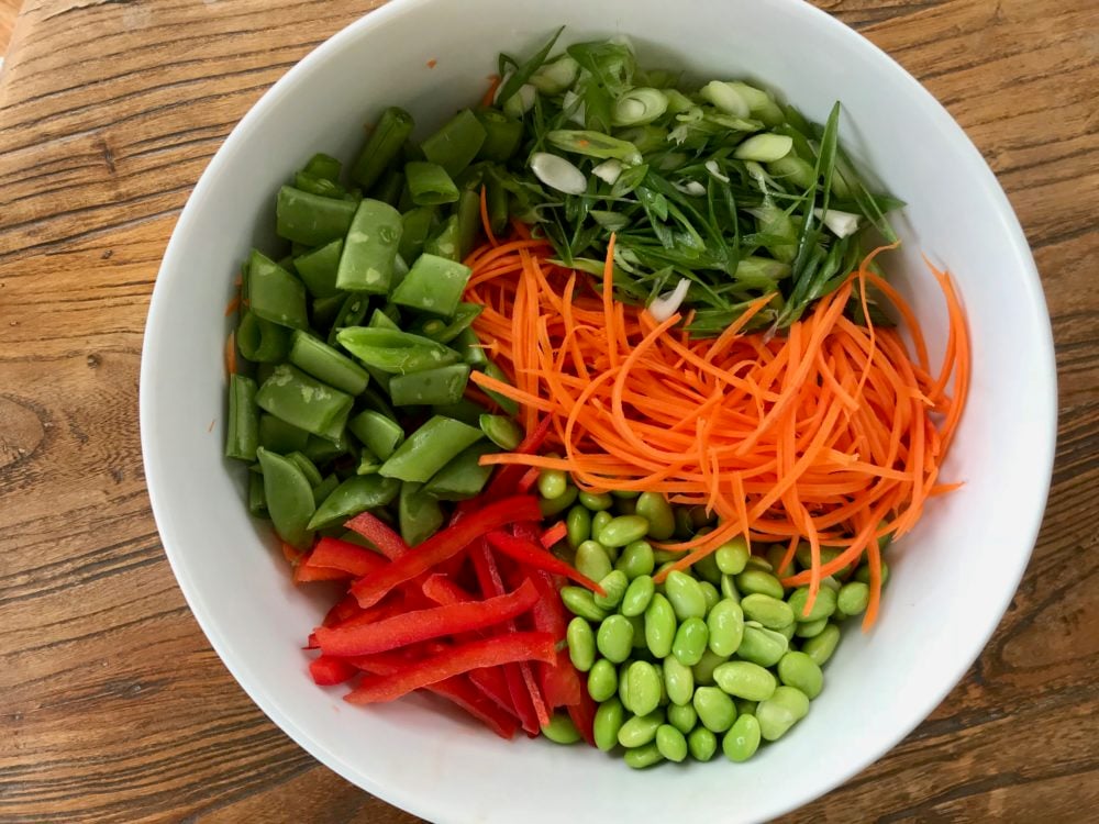 bowl full of prepped veggies: edamame, carrots, red peppers, scallions, snap peas