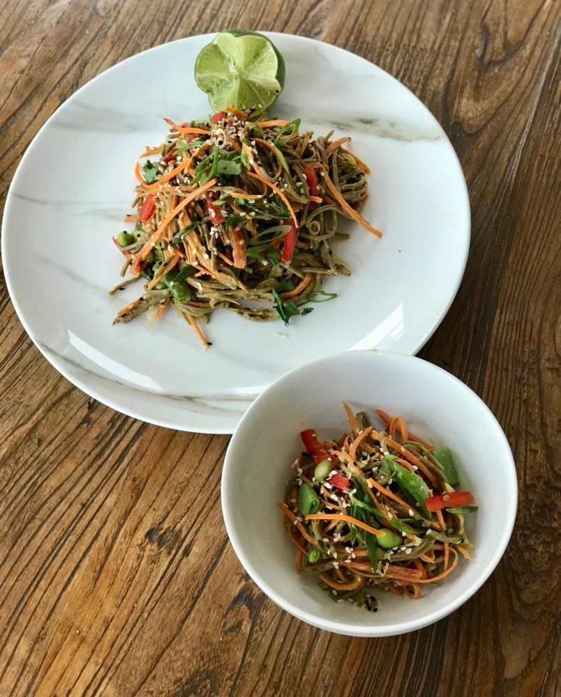 Long soba noodles with brightly colored julienned vegetables on a plate and in a bowl as a salad.