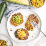 Zucchini Corn Fritters on a small white plate. One with sliced jalapenos, one plain and the other has mango salsa on top.
