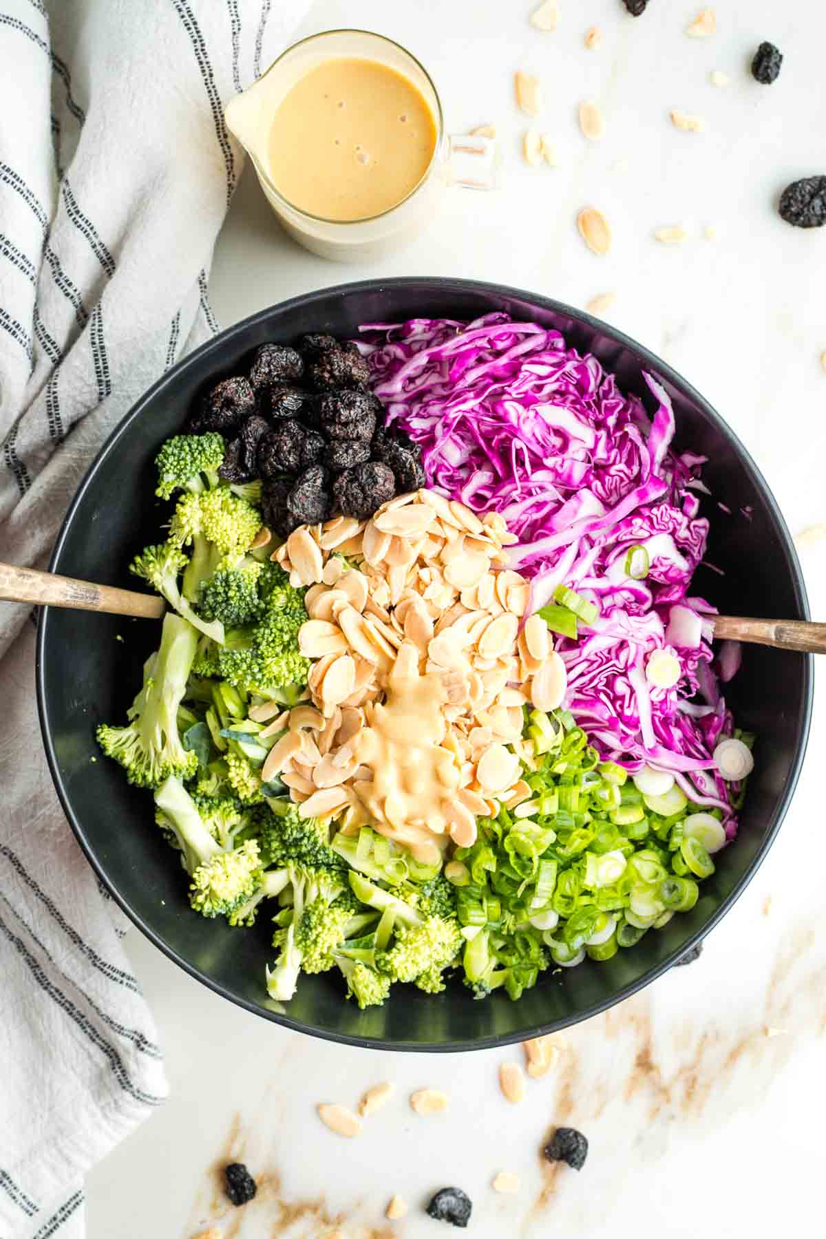 Dressing in the center of a prepped salad with broccoli, cabbage, nuts, dried fruit and scallions.