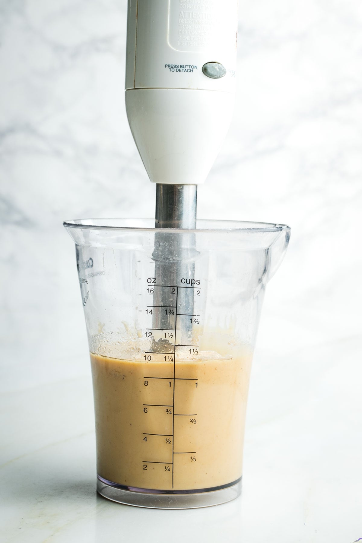 Immersion blender creating a creamy light tan dressing in a cup.