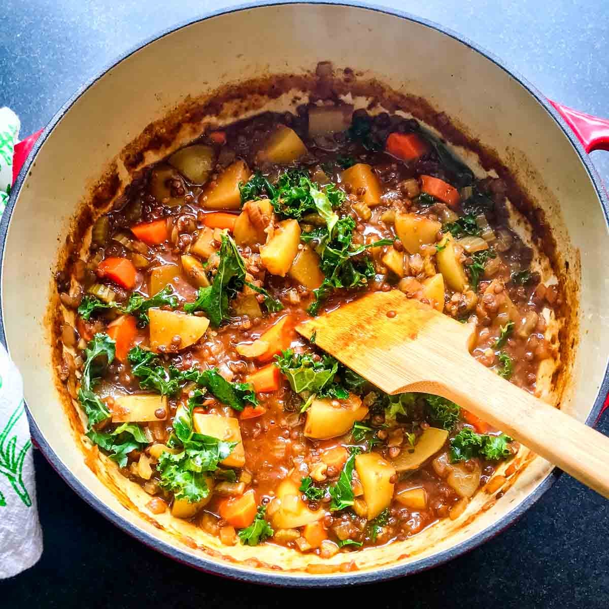 Dutch oven with chunks of potatoes and carrots plus lentils and kale in a tomato sauce.