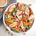 Large white bowl with kale and apple salad, roasted sweet potatoes and figs plus apple vinaigrette