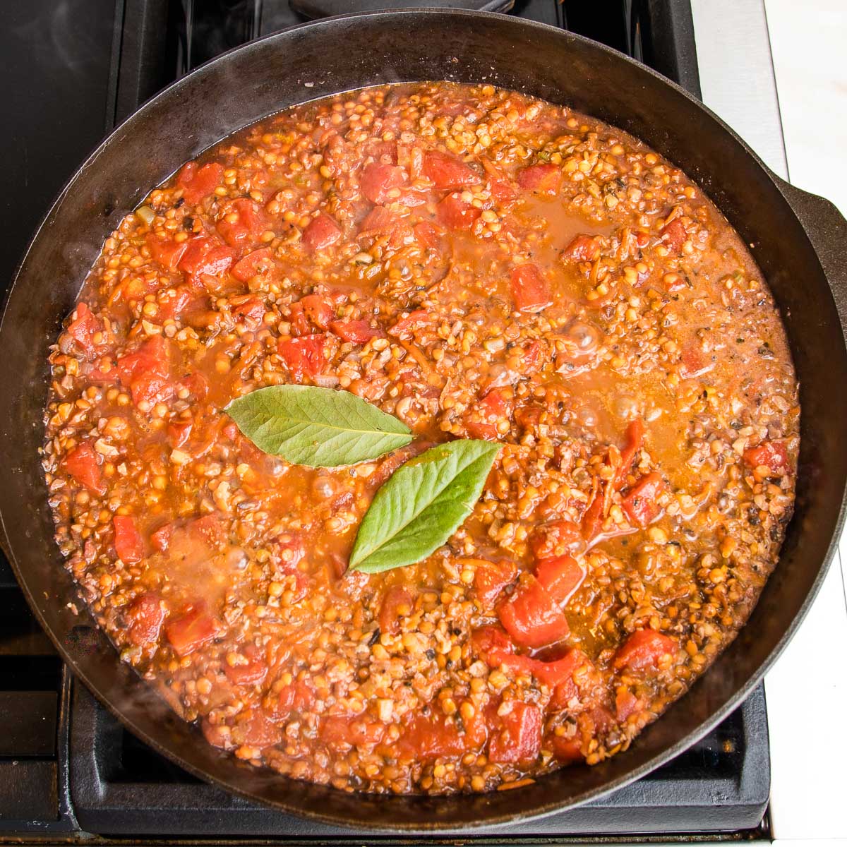 Chunky vegan bolognese, simmering in a cast iron skillet with bay leaves on top.